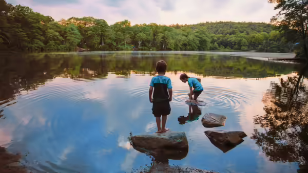 two children standing in a pond looking beneath the water 