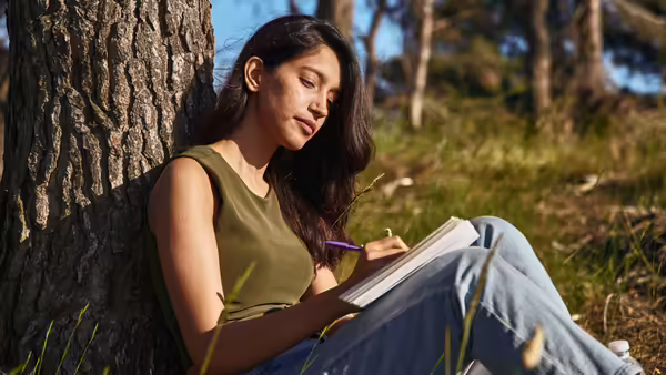 lady sitting next to tree writing