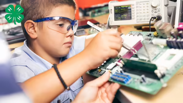 A young boy using larger metal tweezers to work on the inside of a computer. 