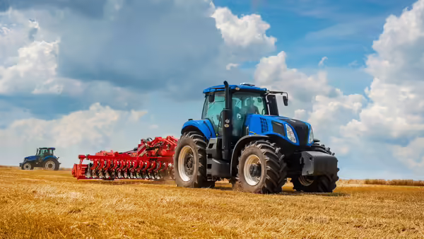 A blue tractor pulling a red hay rake behind it.