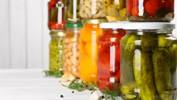 Glass jars with different pickled foods on white wooden background.