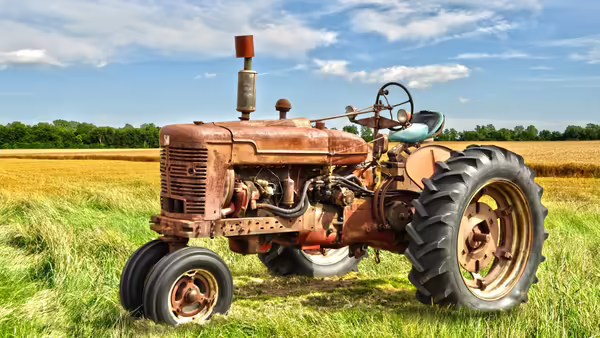 An old red metal tractor, sitting in a field. 