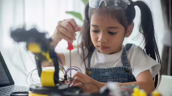 A little girl using a red screwdriver to build a robot.