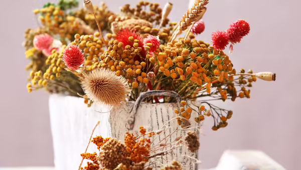 A fall flower arrangment in a white vase.
