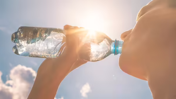 A person outside under the sun taking a drink from their water bottle.