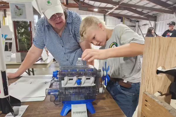 A 4-H member shows a volunteer judge his small engine project