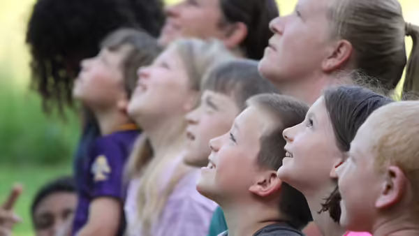 Group of youth and an adult look to the sky with wonder.