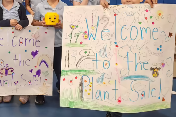 Students hold up signs that say "welcome to the plant sale"