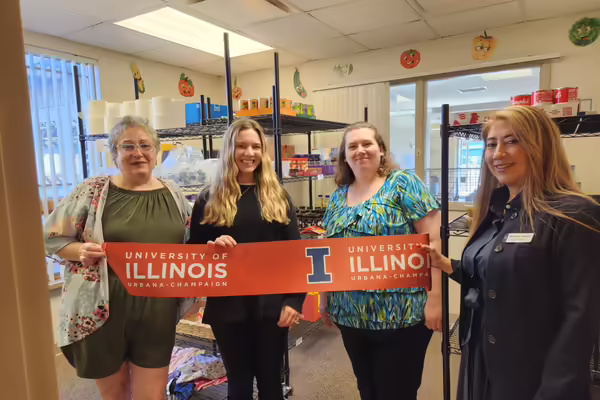 Four people hold up a ribbon inside a food pantry room