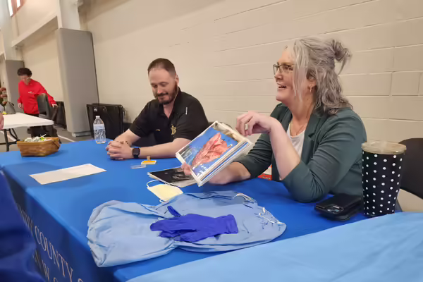 Two people sit at a table, showing images to a group of students