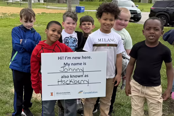 students pose in front of the sign of the tree they planted and named