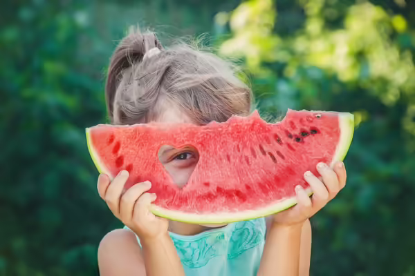 girl looking through hear-shaped hole in a slice of watermelon