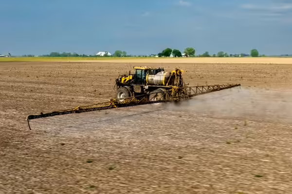 A sprayer traveling across a farm field releasing liquid herbicide. 