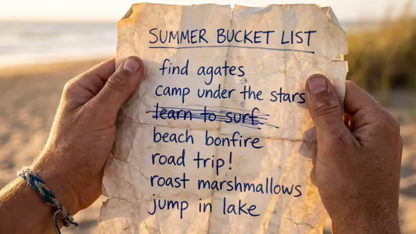 At the beach, a close-up of hands holding a summer bucket list. One item is crossed off.