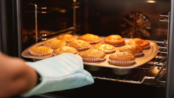 pulling a tray of muffins out of an oven