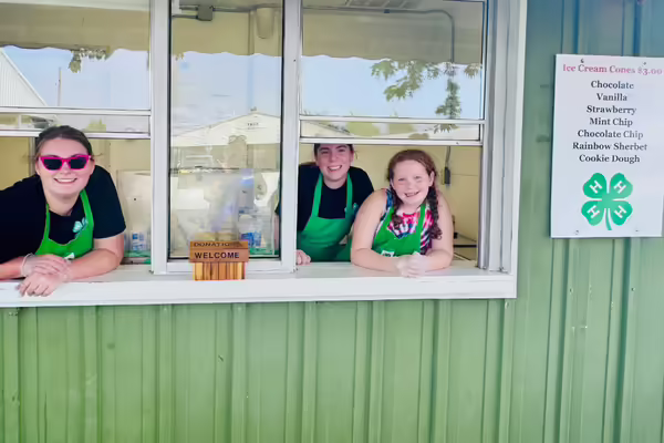 three girls in 4-H aprons in a green building