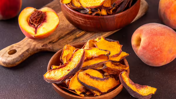 Fresh peaches and sliced dried peaches arranged on a cutting board and in wooden bowls.