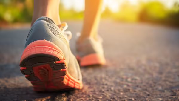 A close-up view of athletic shoes walking on a paved path outdoors, with one shoe in sharp focus and the other blurred in the background. 