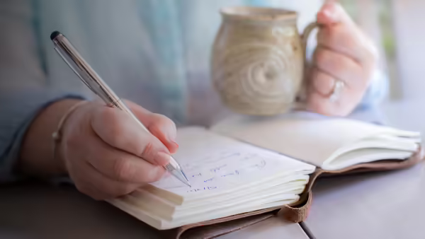 A woman dringing coffee, writing her life story in a notebook.