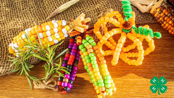 Fall-themed beaded corn and pumpkin ornaments resting on a wooden table with burlap.