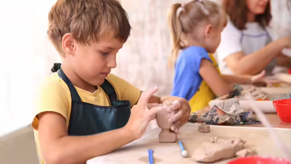 young kids modeling clay at a table with bowls and supplies nearby