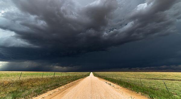 dirt road leading toward a dark cloudy stormy sky