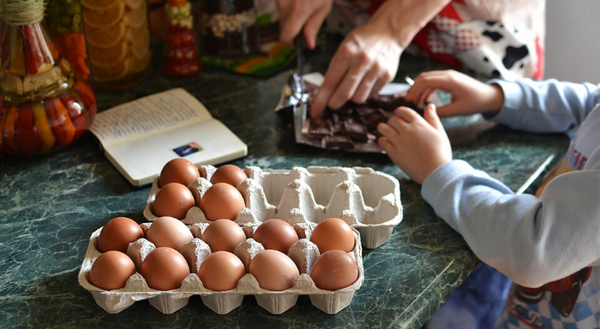 Child and parent arms around table with carton of eggs. 