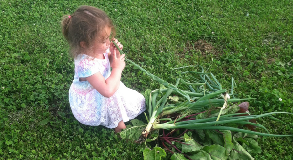 A young girl sits in grass with a pile of harvested vegetables