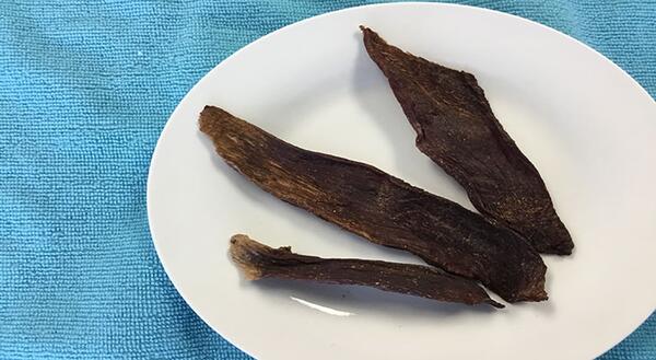 Three strips of jerky on white plate with blue background
