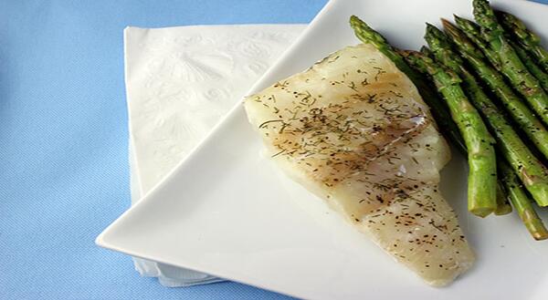 Dill coated white fish and asparagus on white plate and blue background