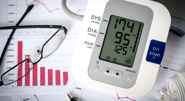 Image of blood pressure reading with 174 systolic and 95 diastolic. Sitting on a chart showing a blood pressure trend going downward. Also in image is a pair of glasses and a bottle of medication.