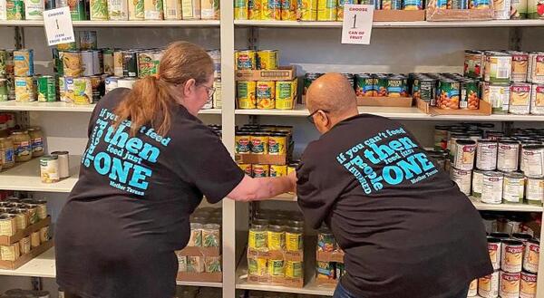 two ladies with their backs to the camera stocking shelves at a food pantry