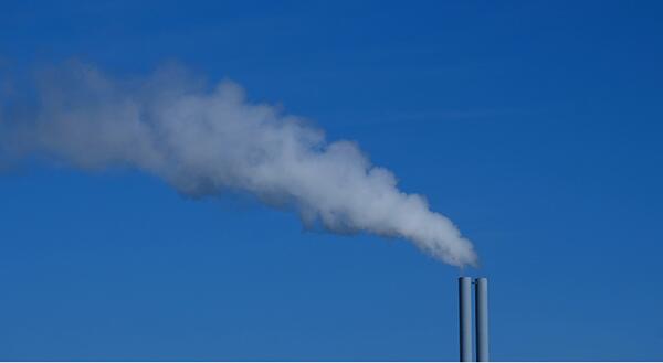 Blue sky with smokestack further away releasing cloudy emissions. 