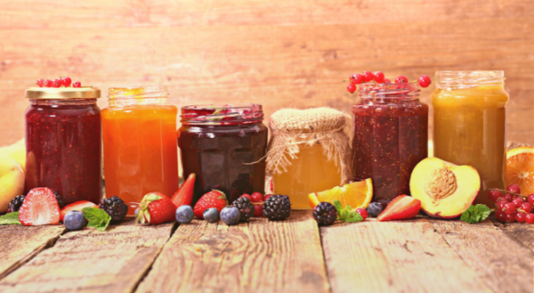 Image of a variety of fruit jams in jars with a variety of fruit and berries scattered in front of the jars