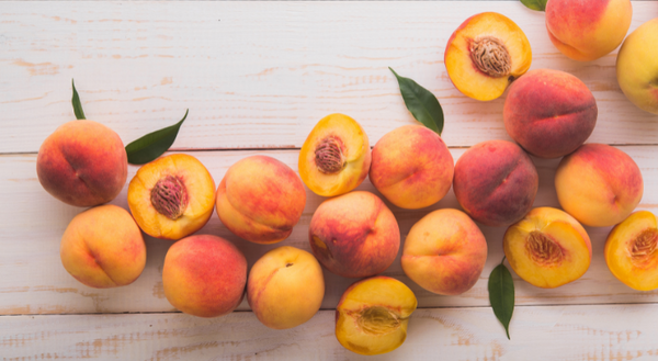 Tan wood background with whole and halved peaches with a few peach leaves