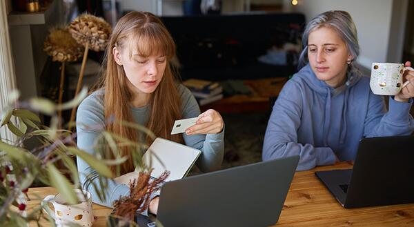 Two woman, one woman looking at credit card and computer