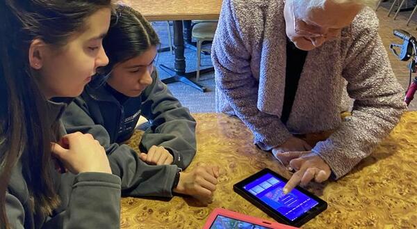 Teens help a senior citizen use an electronic device.
