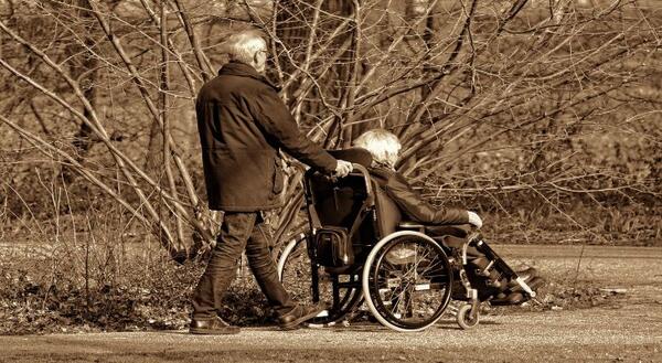 older man pushing older woman in wheelchair