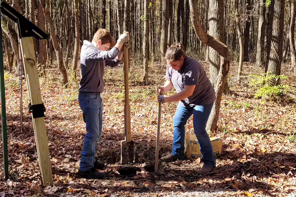 A boy and girl use post hole diggers in a forest