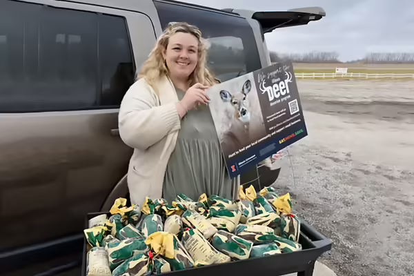Woman outside holds sign in front of packets of frozen venison
