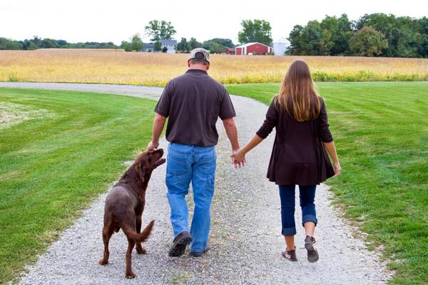 farm couple walks down gravel lane with brown Labrador retriever