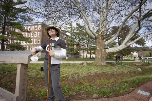 Woman in hat and sunglasses stands in rain garden