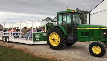 A green tractor pulls a seated trailer full of people around a farm tour