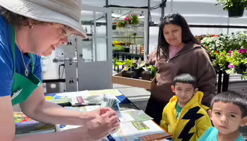 Woman showing two young kids and their mother some gardening information in a greenhouse.
