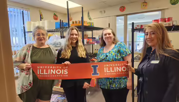 Four people hold up a ribbon inside a food pantry room