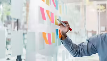 hand with marker writing on sticky notes placed on a transparent wall