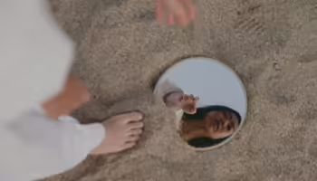 woman looking in mirror that is in sand