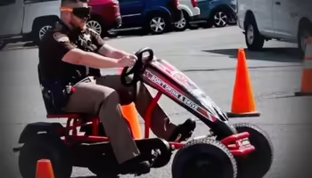 Deputy demonstrating drunk driving by wearing special goggles and driving a cart through orange cones