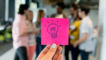 hand holding sticky note with light bulb on it in front of students