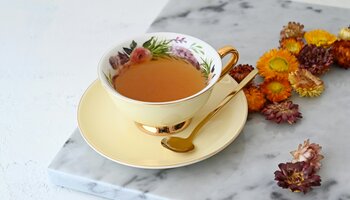 tea cup with flowers with liquid in it spoon on saucer with dried flowers around it